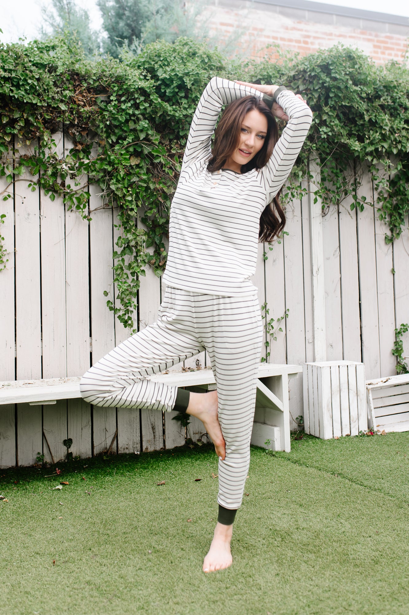 Model in Women’s Ribbed Henley Set in Fir Stripe, standing on one leg with arms overhead.