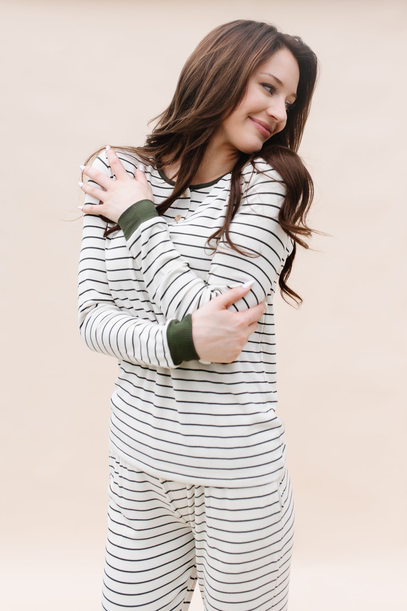 Model looking to the side while hugging herself while wearing the Kyte Women’s Ribbed Henley Set in Fir Stripe