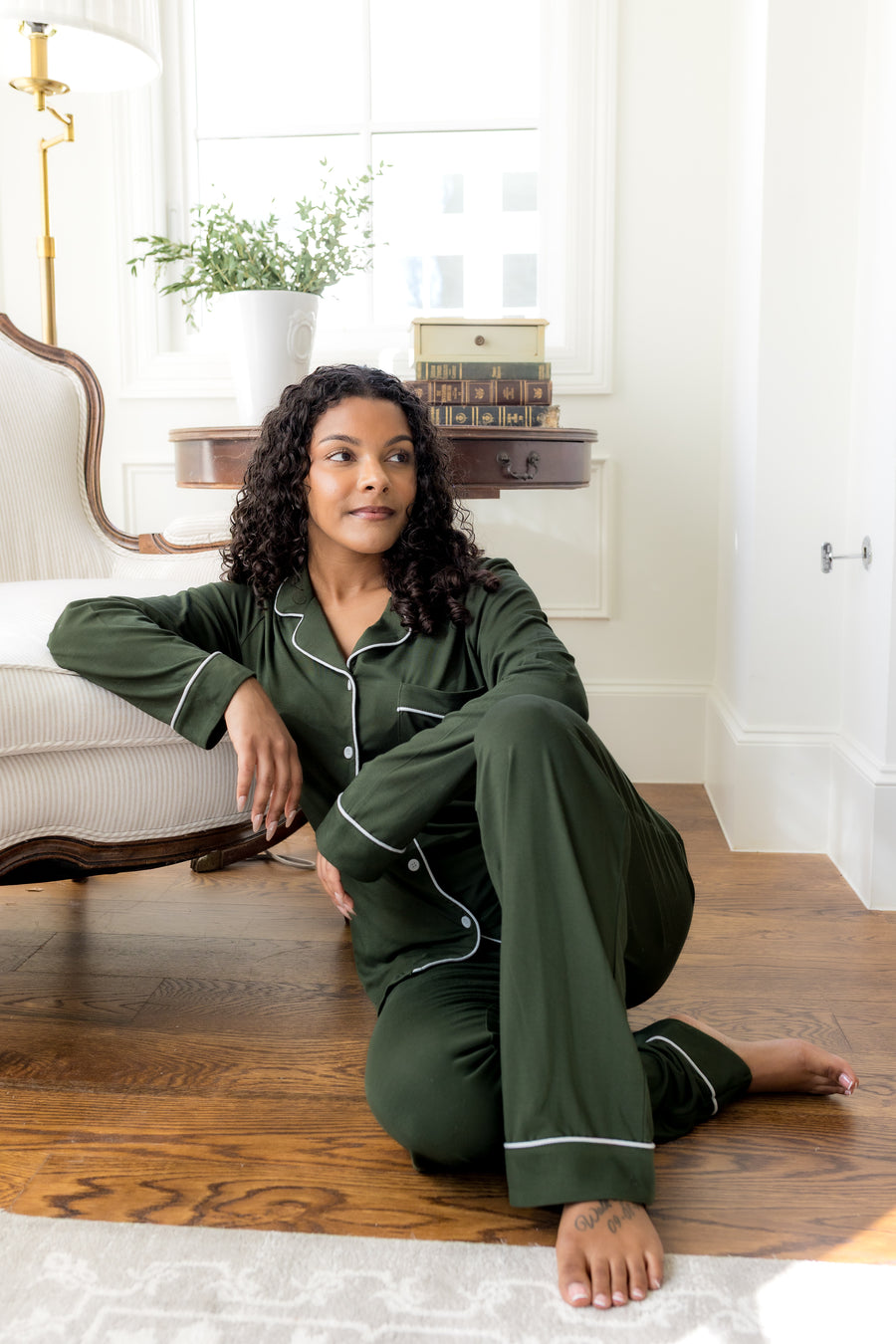 Woman in green pajamas sitting on a wooden floor in a bright room.
