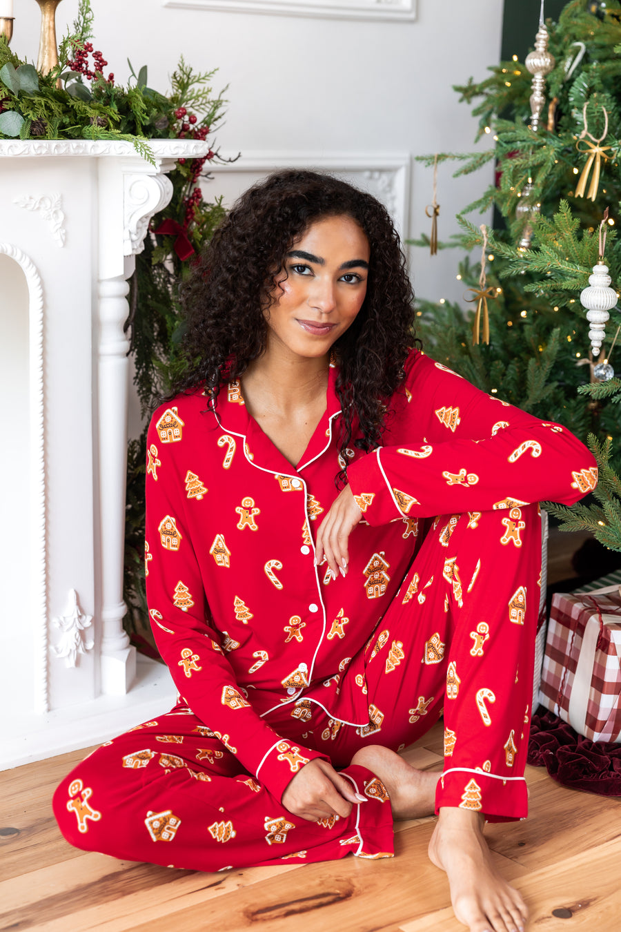 Woman sitting down with one leg propped up and the other bent in with her arm on her knee in long sleeve pajama set in gingerbread print