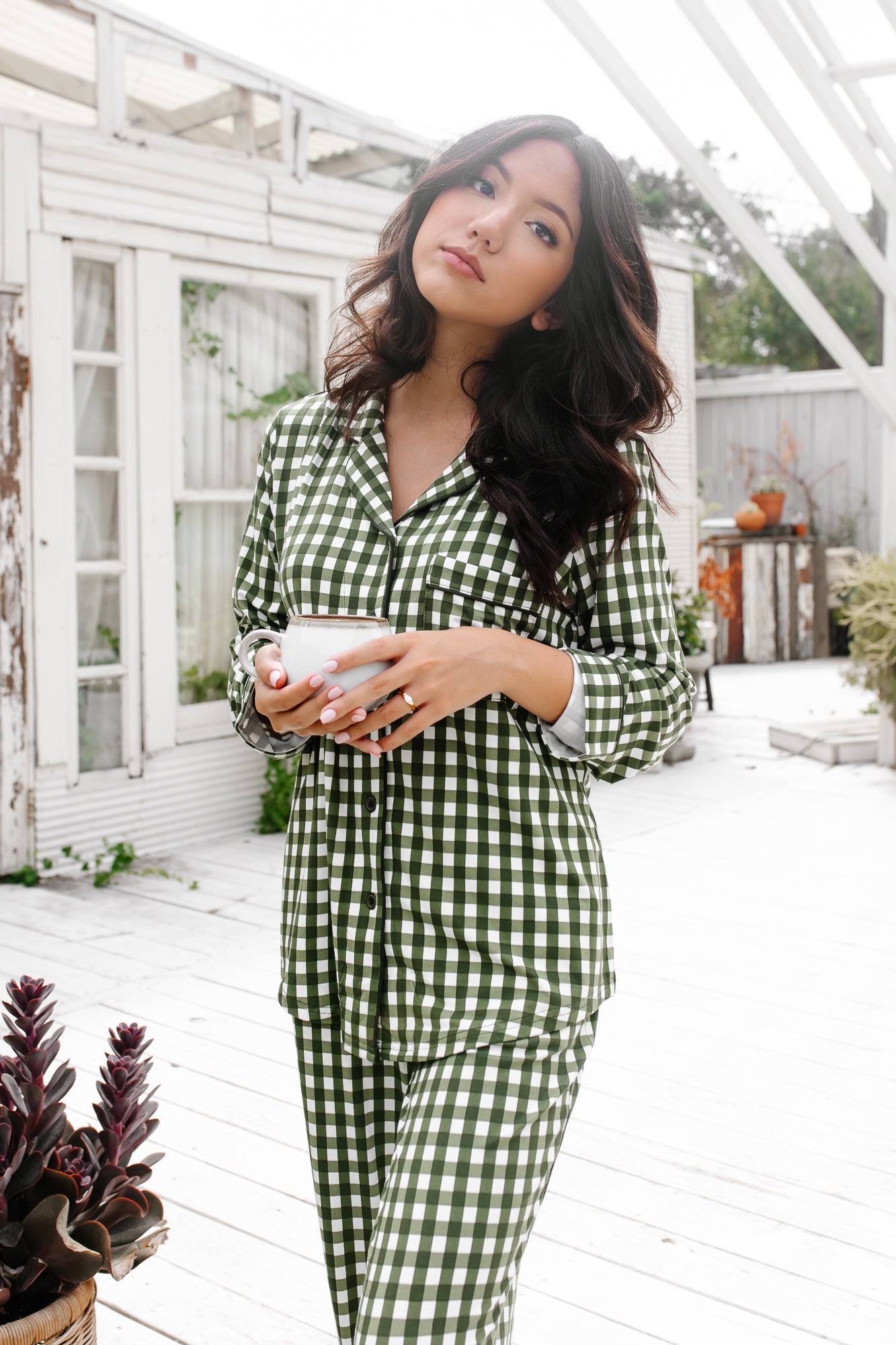 Woman wearing a green and white checkered outfit standing outdoors holding coffee cup