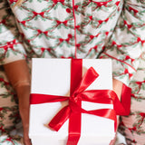 Close up of the Kyte Bamboo Long-Sleeved Women's Pajama Set in Holiday Bow while holding a gift with a red bow