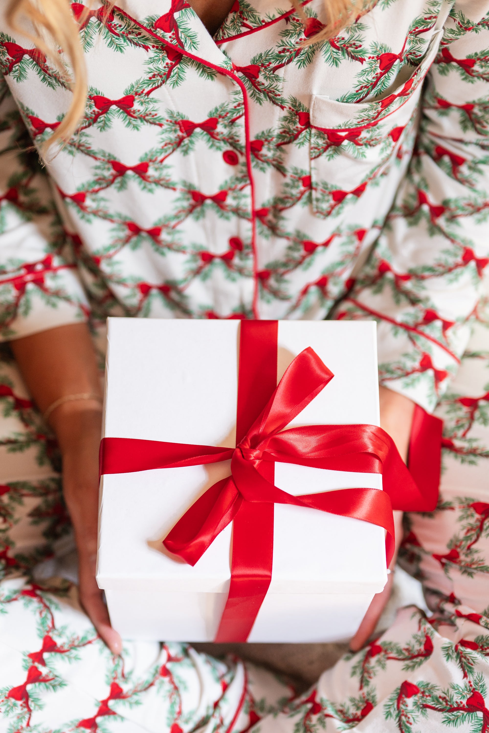Close up of the Kyte Bamboo Long-Sleeved Women's Pajama Set in Holiday Bow while holding a gift with a red bow