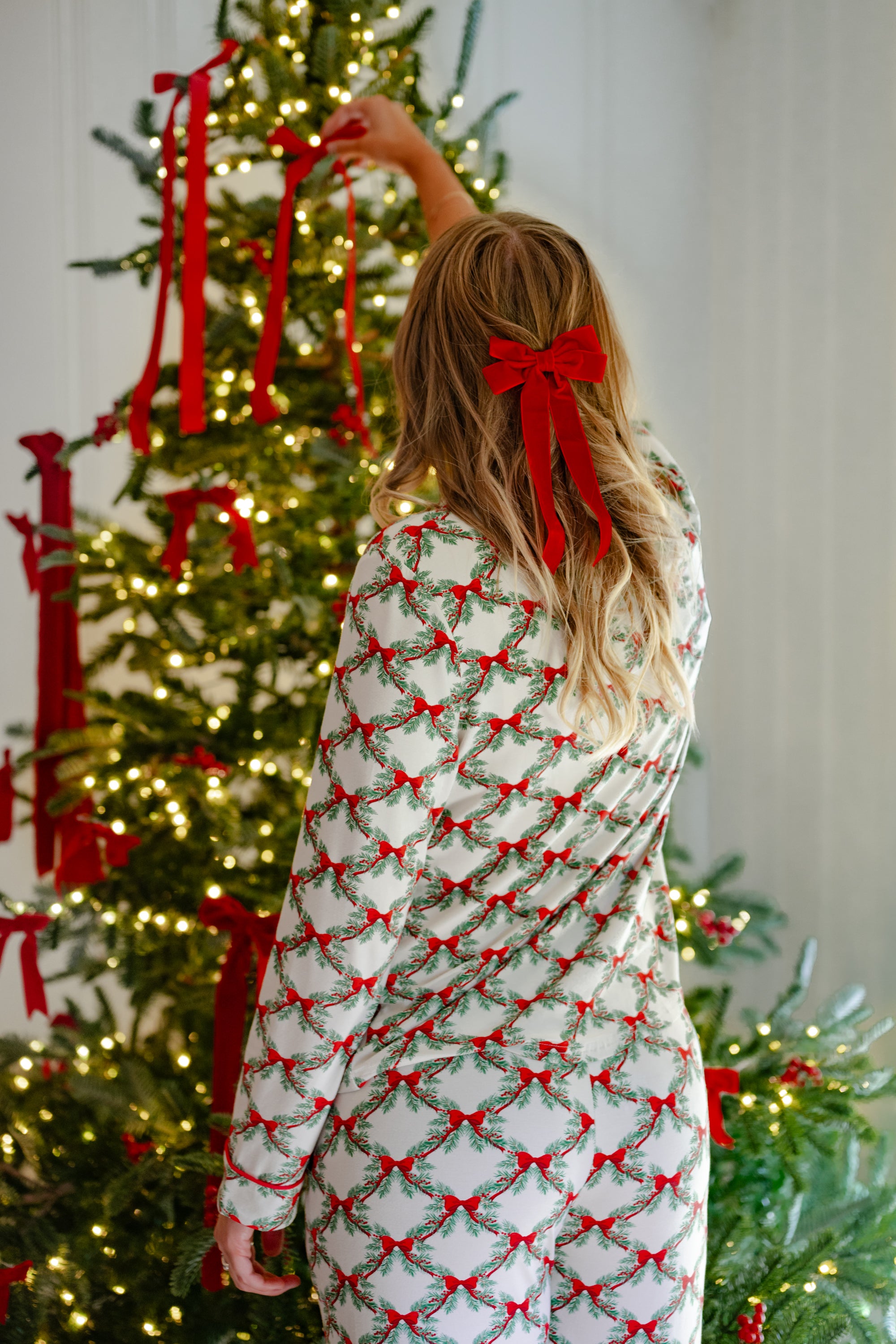 Woman putting a bow on a Christmas tree while modeling the back of the Bamboo Long-Sleeved Women's Pajama Set in Holiday Bow