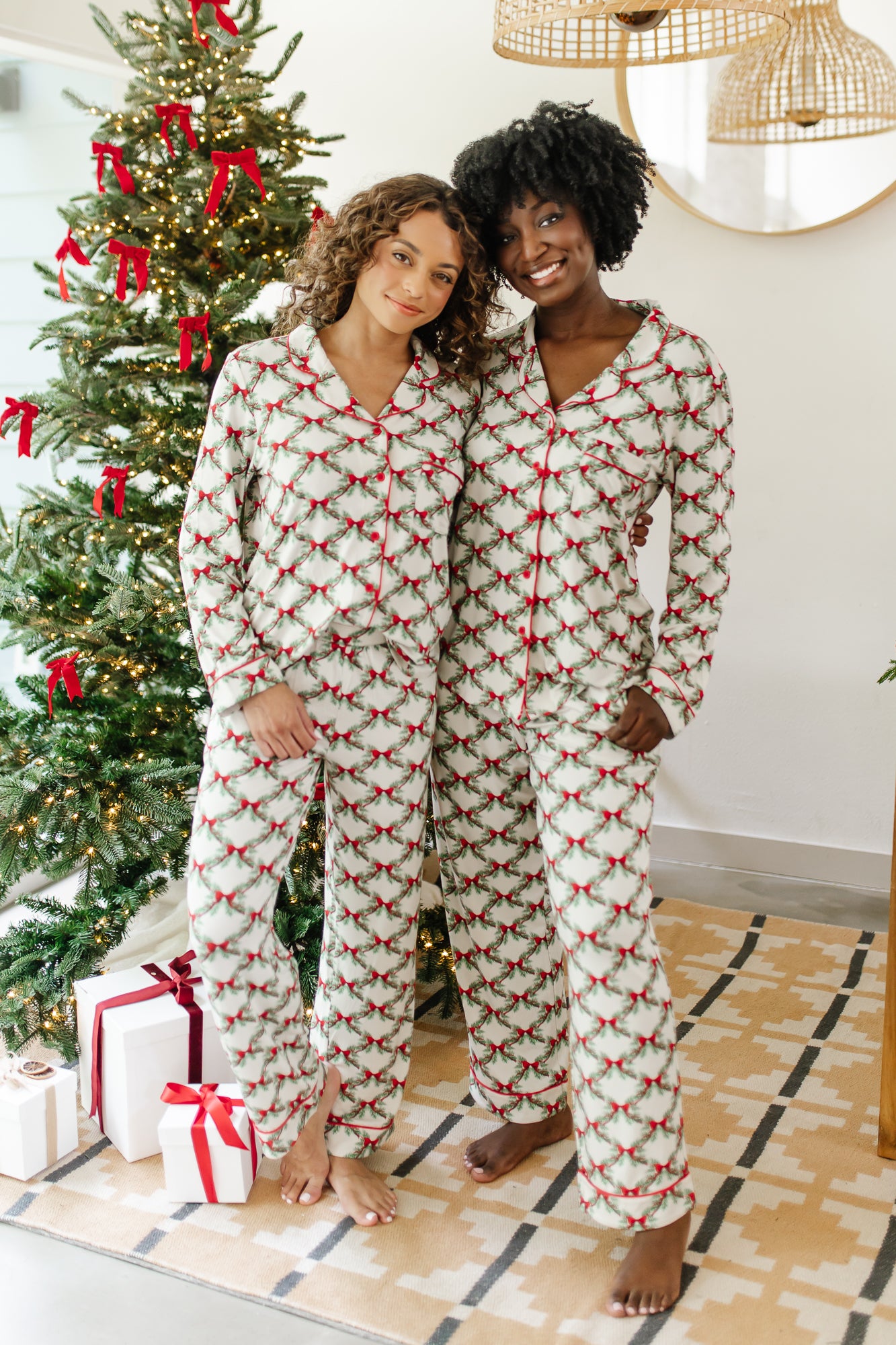 Models standing in front of a Christmas tree with arms around each other while wearing matching Bamboo Long-Sleeved Women's Pajama Set in Holiday Bow
