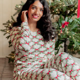 Smiling female model sitting on the floor wearing the Women's Jogger Pajama Set in Holiday Bow in front of a decorated Christmas Tree