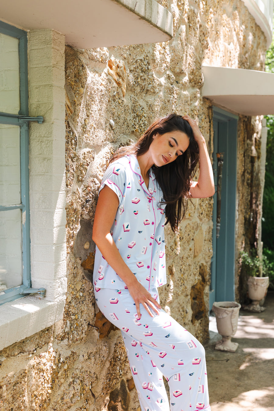 Woman wearing a light blue pajama set with mahjong pattern sitting on a stone wall.