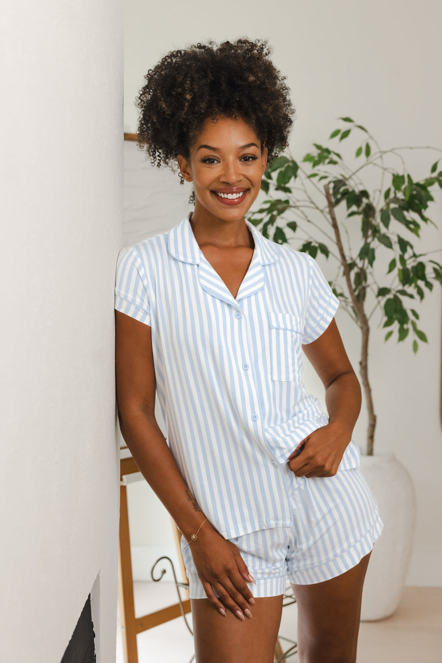 Smiling woman leaning on a wall while modeling the Kyte Women's Short Sleeve Pajama Set in Small Mist Stripe