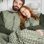 Two people wearing green and white checkered sleep bag walkers sitting on a couch.