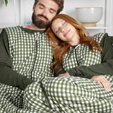 Two people wearing green and white checkered sleep bag walkers sitting on a couch.