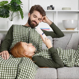 Two people in matching green checkered sleep bag walkers lying on a couch, with one person holding a book.
