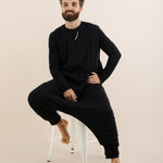 Man wearing a black outfit sitting on a chair against a beige background