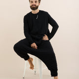 Man wearing a black outfit sitting on a chair against a beige background