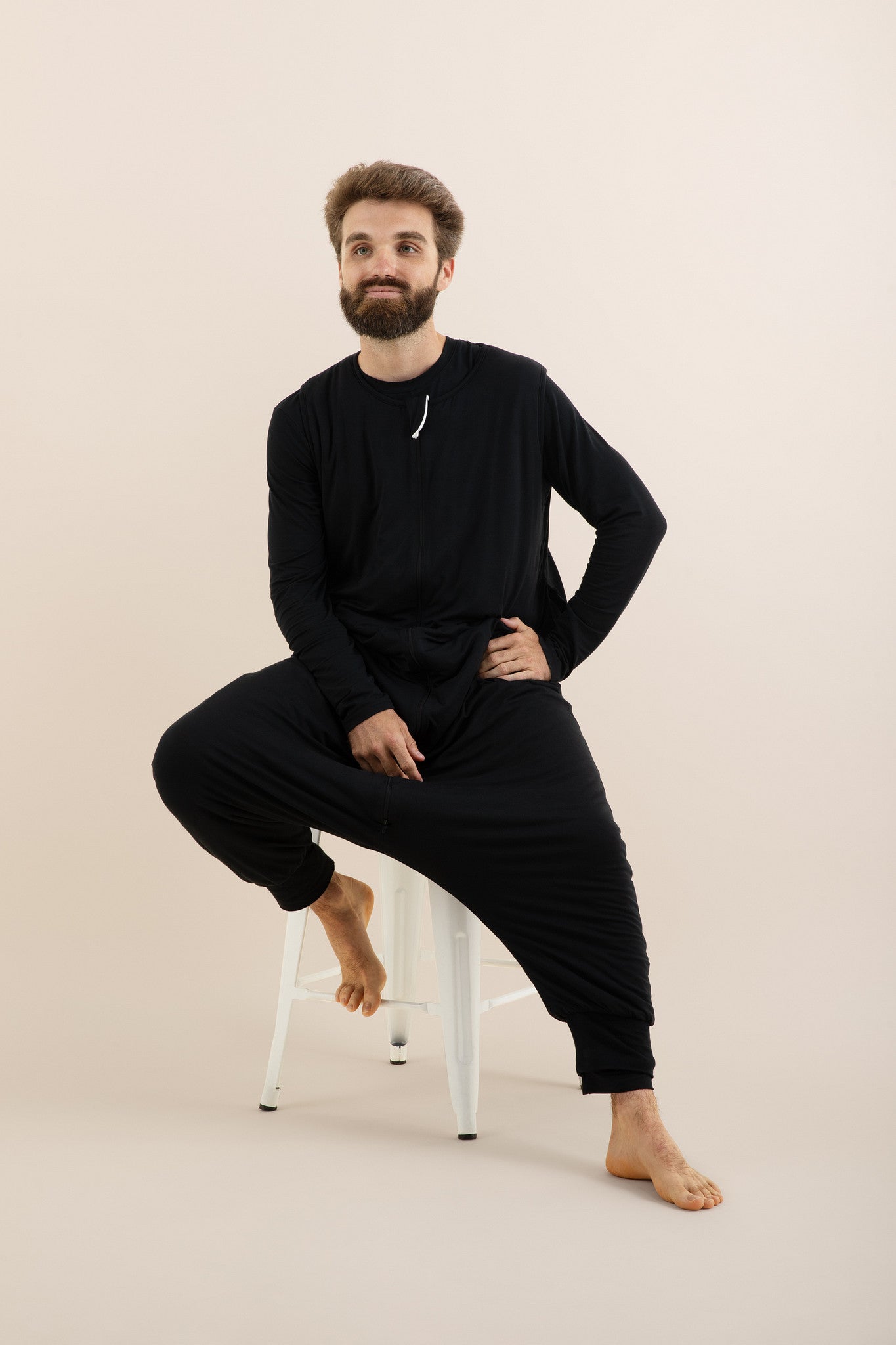 Man wearing a black outfit sitting on a chair against a beige background