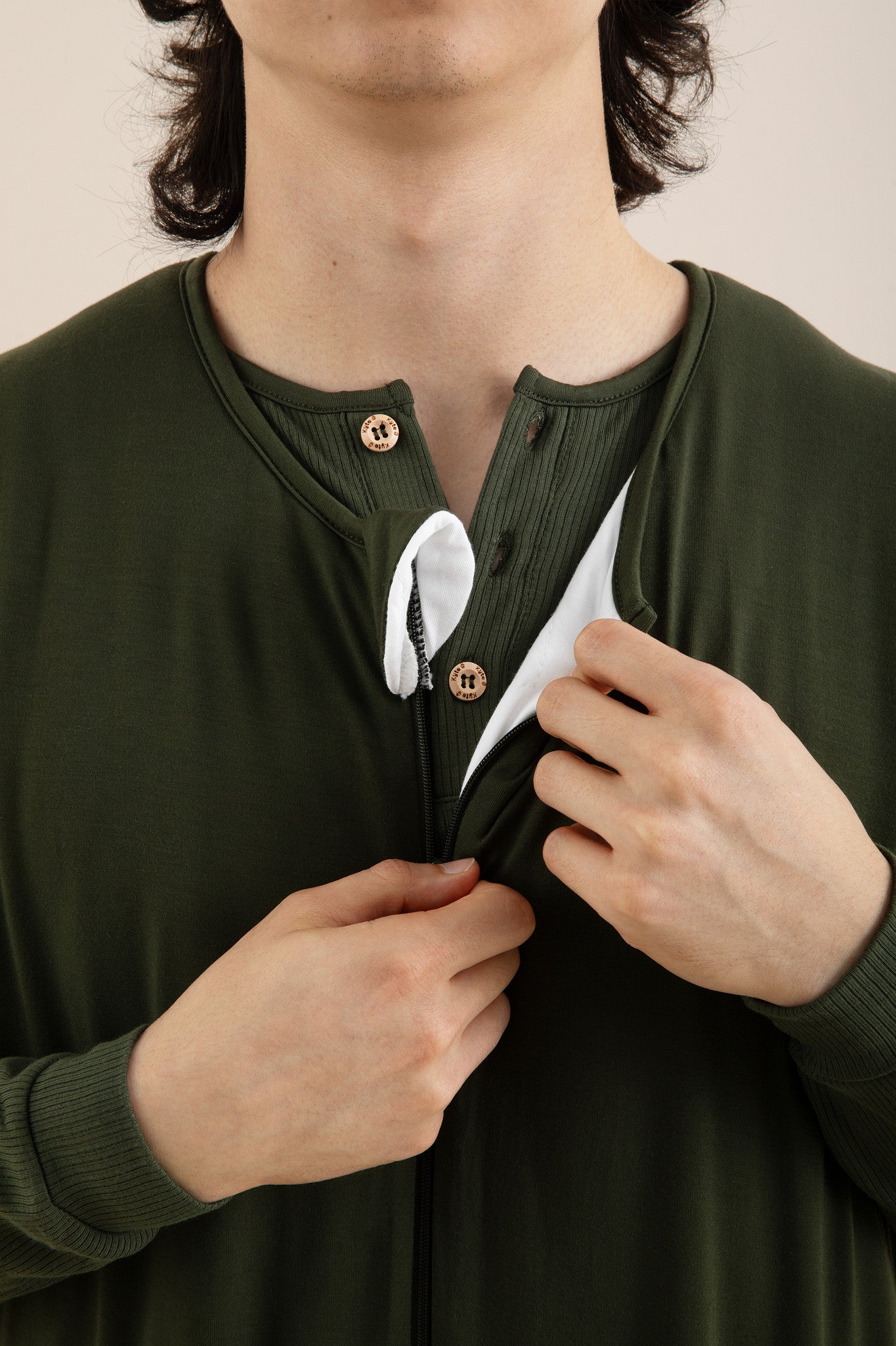 Person wearing a green long-sleeve shirt with buttons, adjusting the collar.