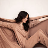 Smiling model holding Bamboo Quilt Blanket in Latte 2.5 open while matching in the Long Sleeve Pajama Set in Latte