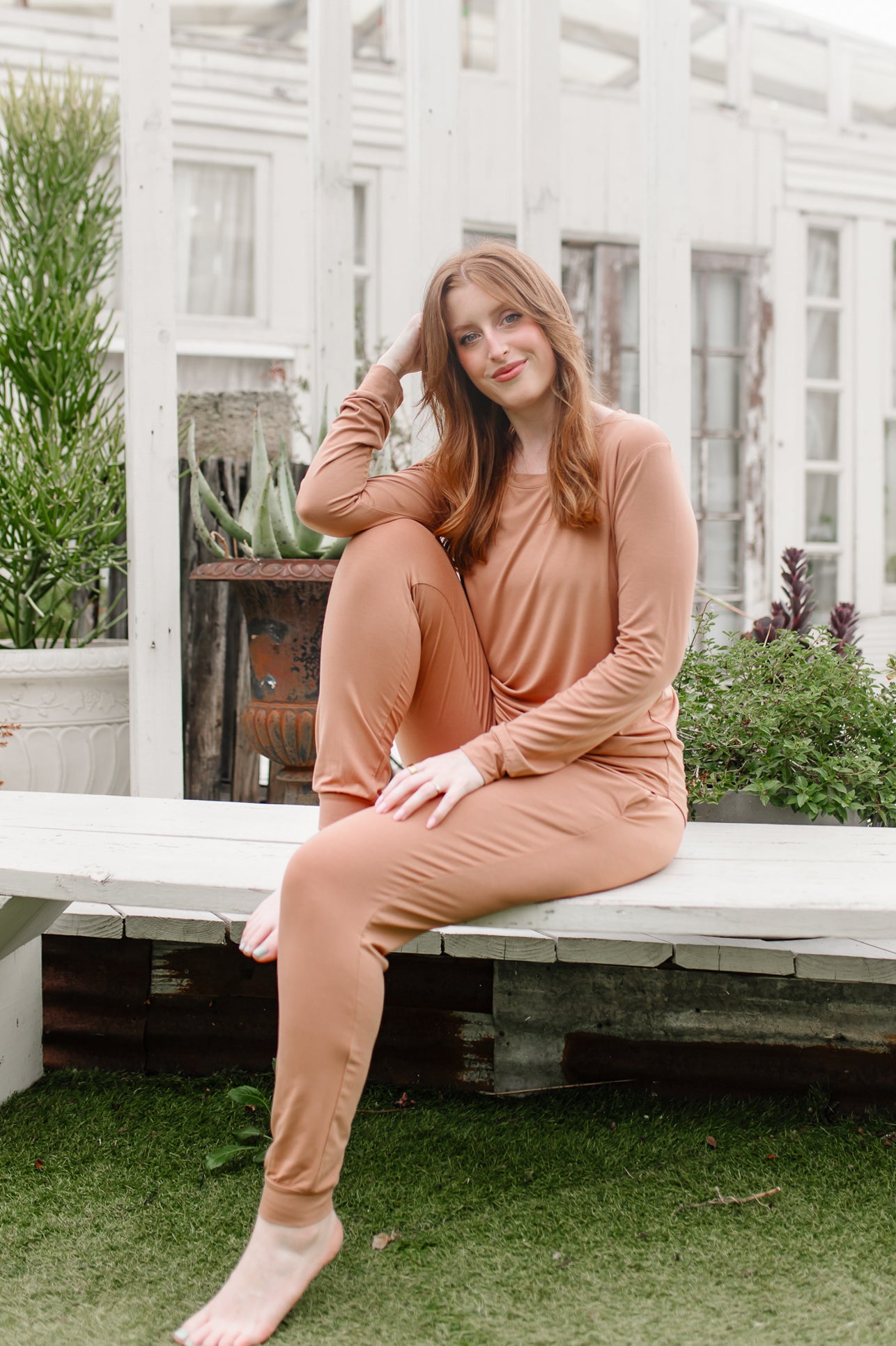 Woman sitting on a wooden bench wearing a bamboo matching set in a medium orange brown called Latte