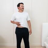 Man modeling Men's Lounge Pants in Midnight and Snow Crew Neck Tee. Slightly pulling up bottom of shirt to show the drawstring of pants.