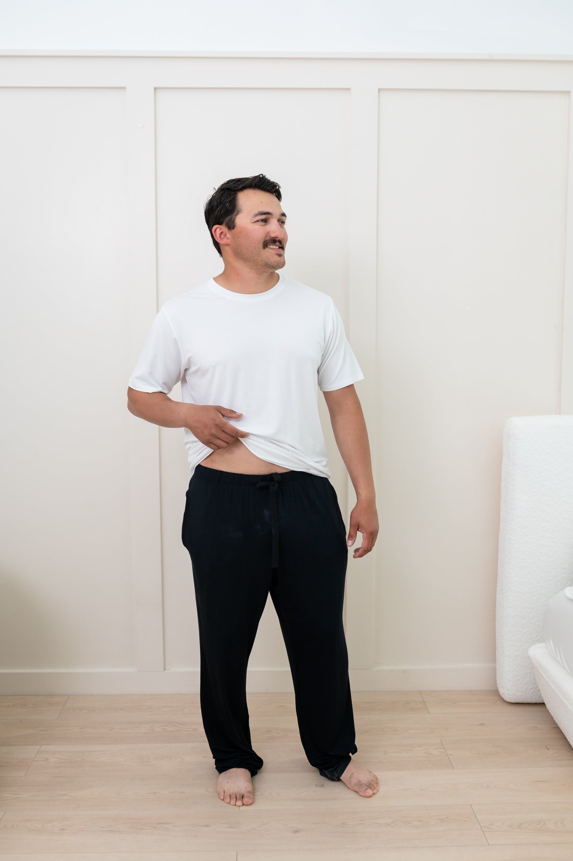 Man modeling Men's Lounge Pants in Midnight and Snow Crew Neck Tee. Slightly pulling up bottom of shirt to show the drawstring of pants.