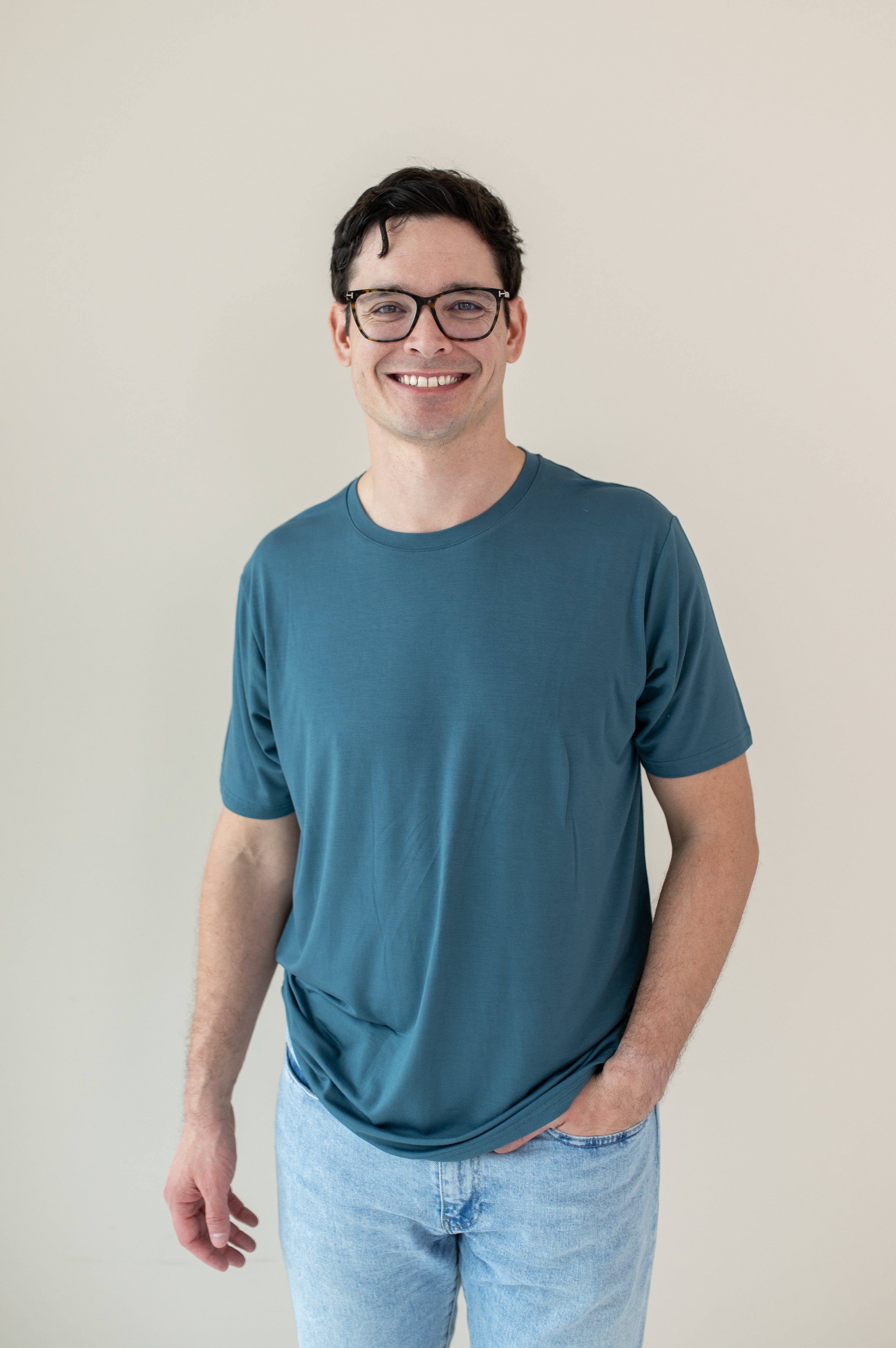 A smiling man in glasses wearing a Kyte Men's Crew Neck in Atlantic and light blue jeans