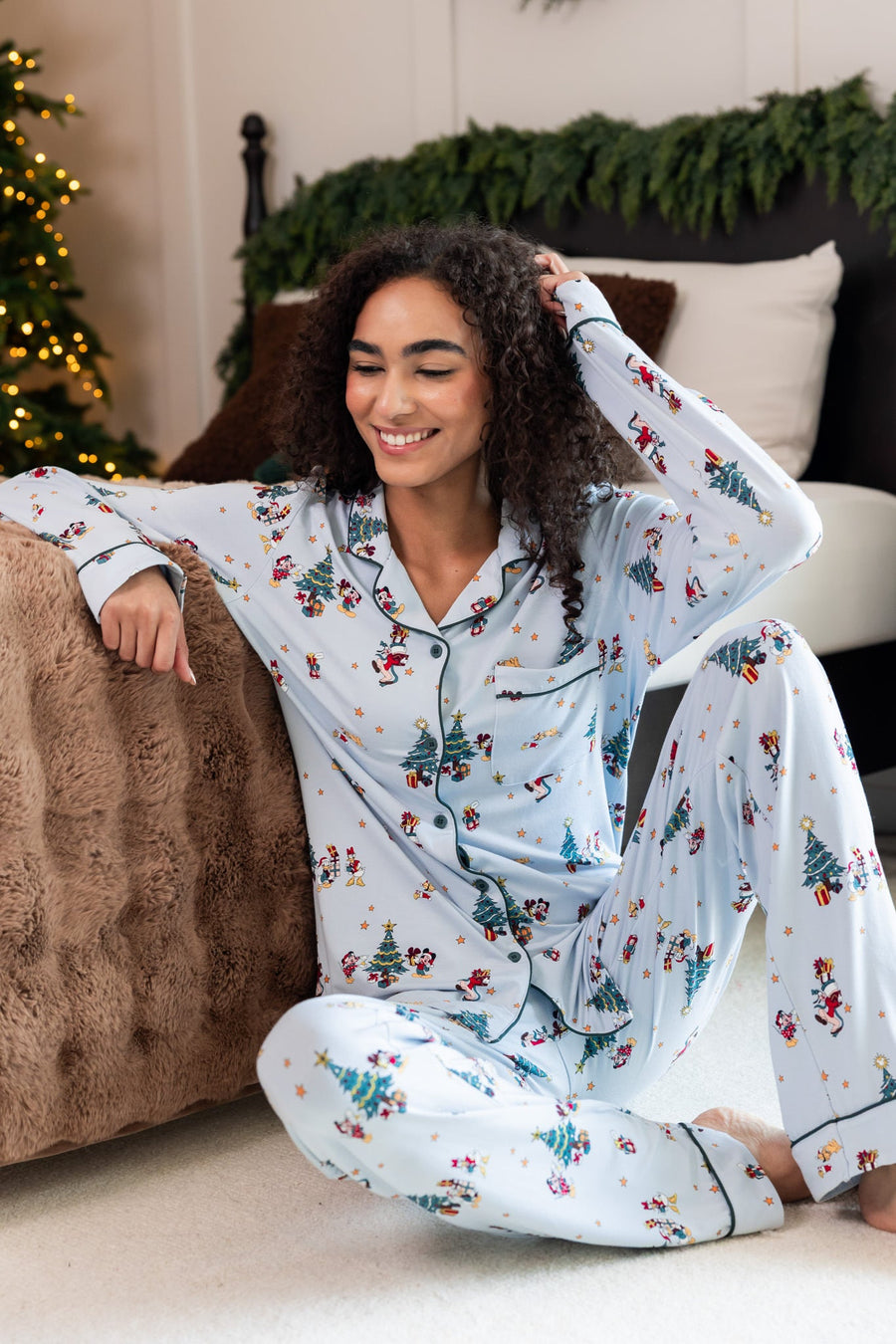 Woman sitting near bed while wearing Long-Sleeved Women's Pajama Set in Mickey & Friends Christmas print