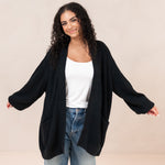 Woman wearing a black cardigan over a white top and blue jeans on a beige background