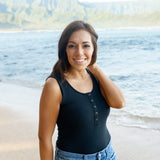 Smiling female on the beach wearing the Women’s Ribbed Henley Bodysuit in Midnight in jean shorts
