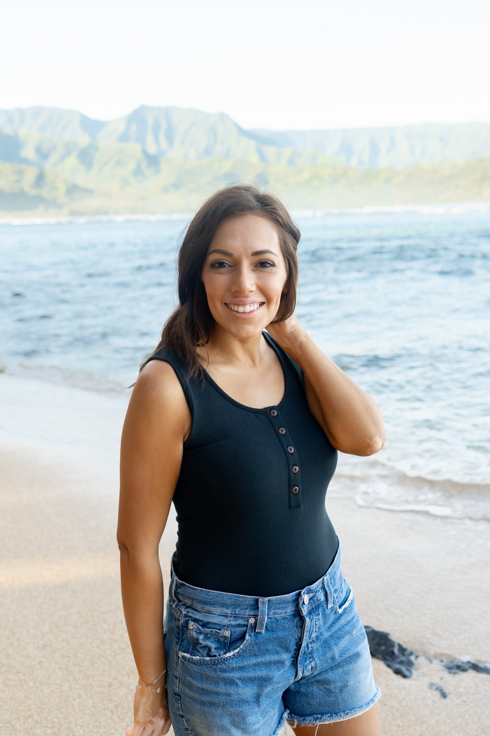 Smiling female on the beach wearing the Women’s Ribbed Henley Bodysuit in Midnight in jean shorts