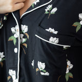 Woman modeling black long sleeve button up pajamas in a magnolia print showing collar and shirt pocket