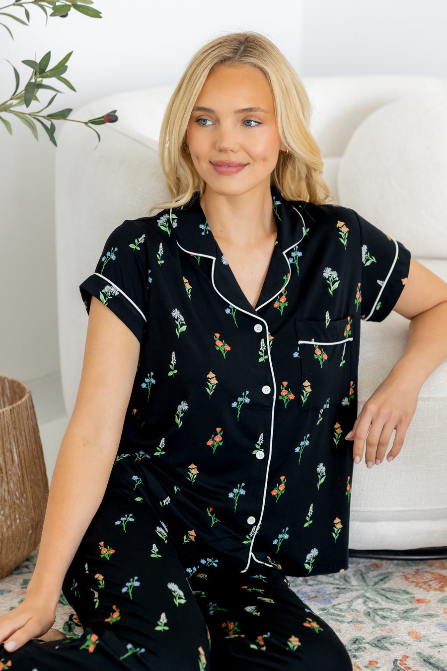 Model sitting on floor wearing Women's Short Sleeve Cropped Pajama Set in Midnight Wildflower print against a white couch