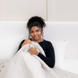 Model laying in bed with the Adult Quilted Blanket in Oat 1.0 overtop her