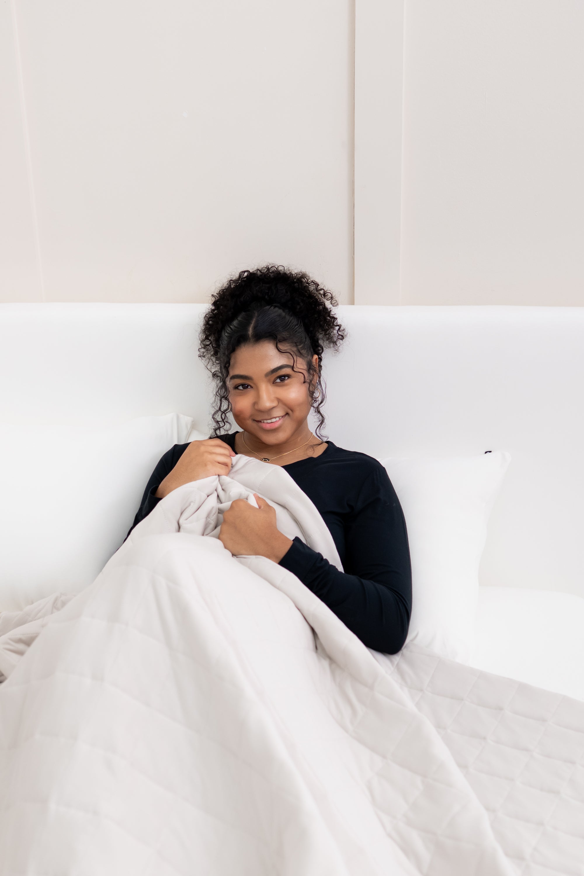 Model laying in bed with the Adult Quilted Blanket in Oat 1.0 overtop her