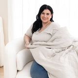 Model sitting in a chair with the Adult Quilted Blanket in Oat 2.5 overtop of her