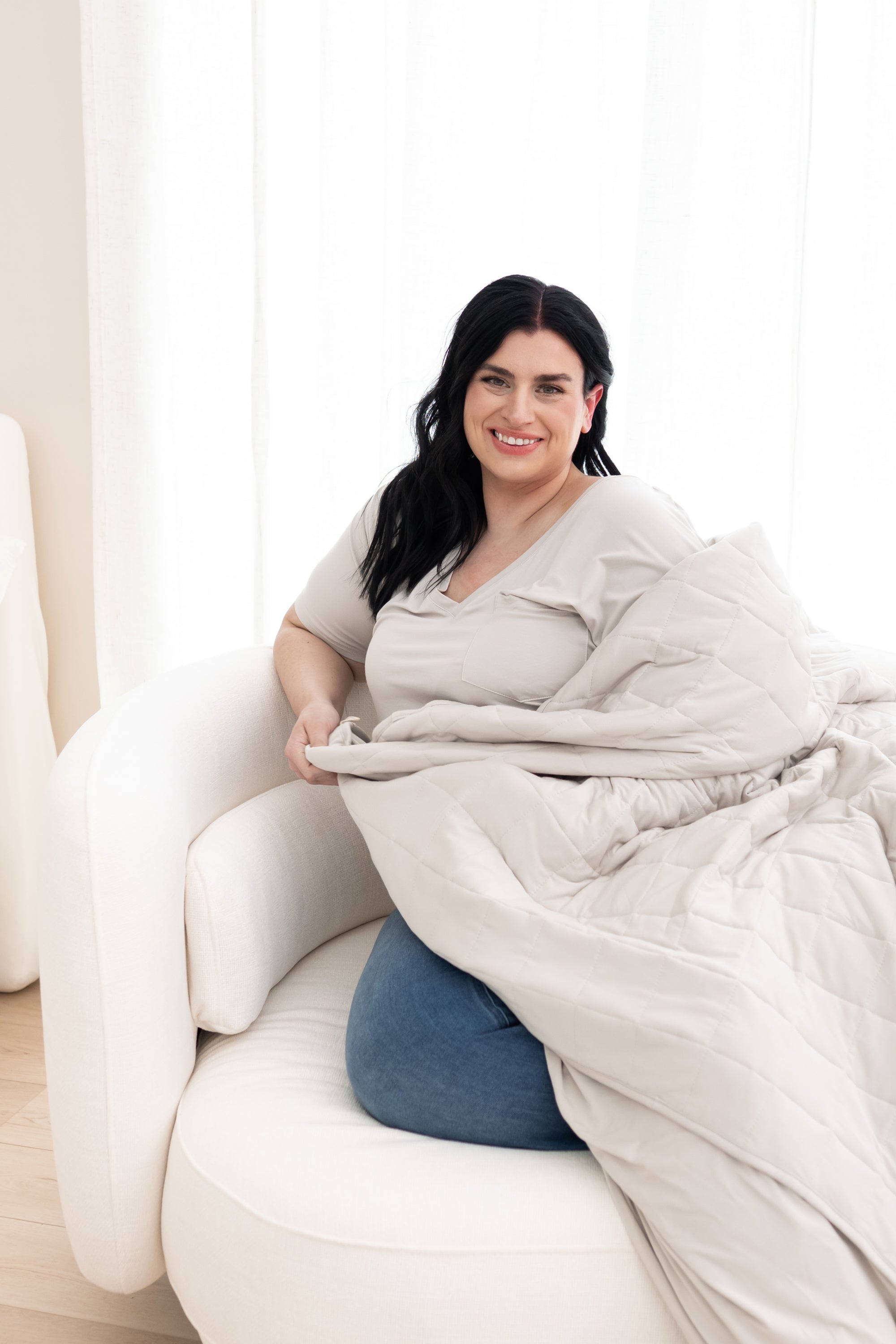 Model sitting in a chair with the Adult Quilted Blanket in Oat 2.5 overtop of her