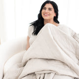 Model sitting on a chair with the Adult Quilted Blanket in Oat 2.5 on top of her