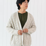 Male model wearing the Chunky Cable Knit Cardigan in Oat paired with Henley and dark pants