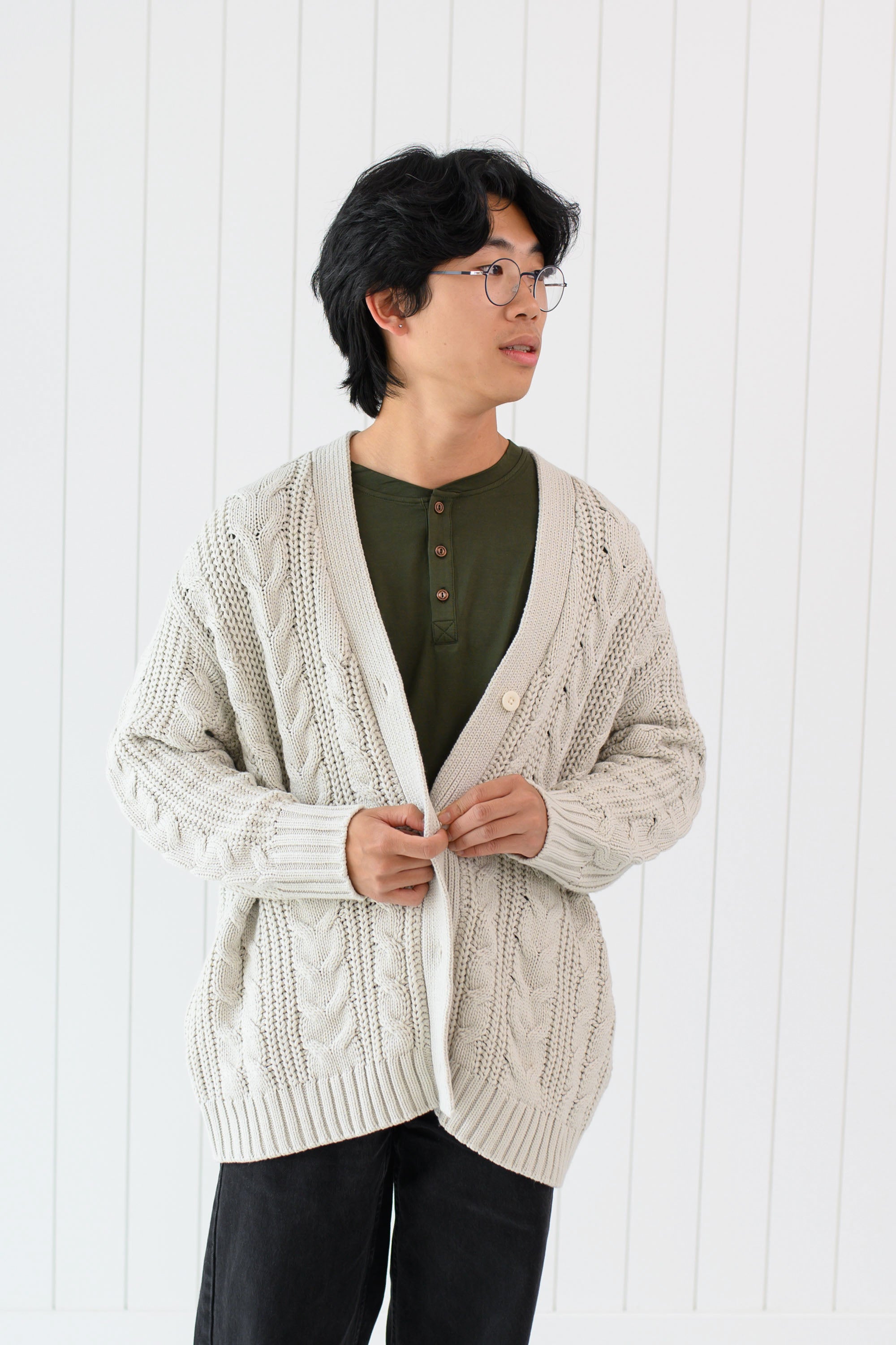 Male model wearing the Chunky Cable Knit Cardigan in Oat paired with Henley and dark pants