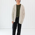 Man standing in a white room while modeling the Chunky Cable Knit Cardigan in Oat