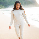 Model in the sand on the beach wearing Kyte Baby Women's Jogger Pajama Set in Oat