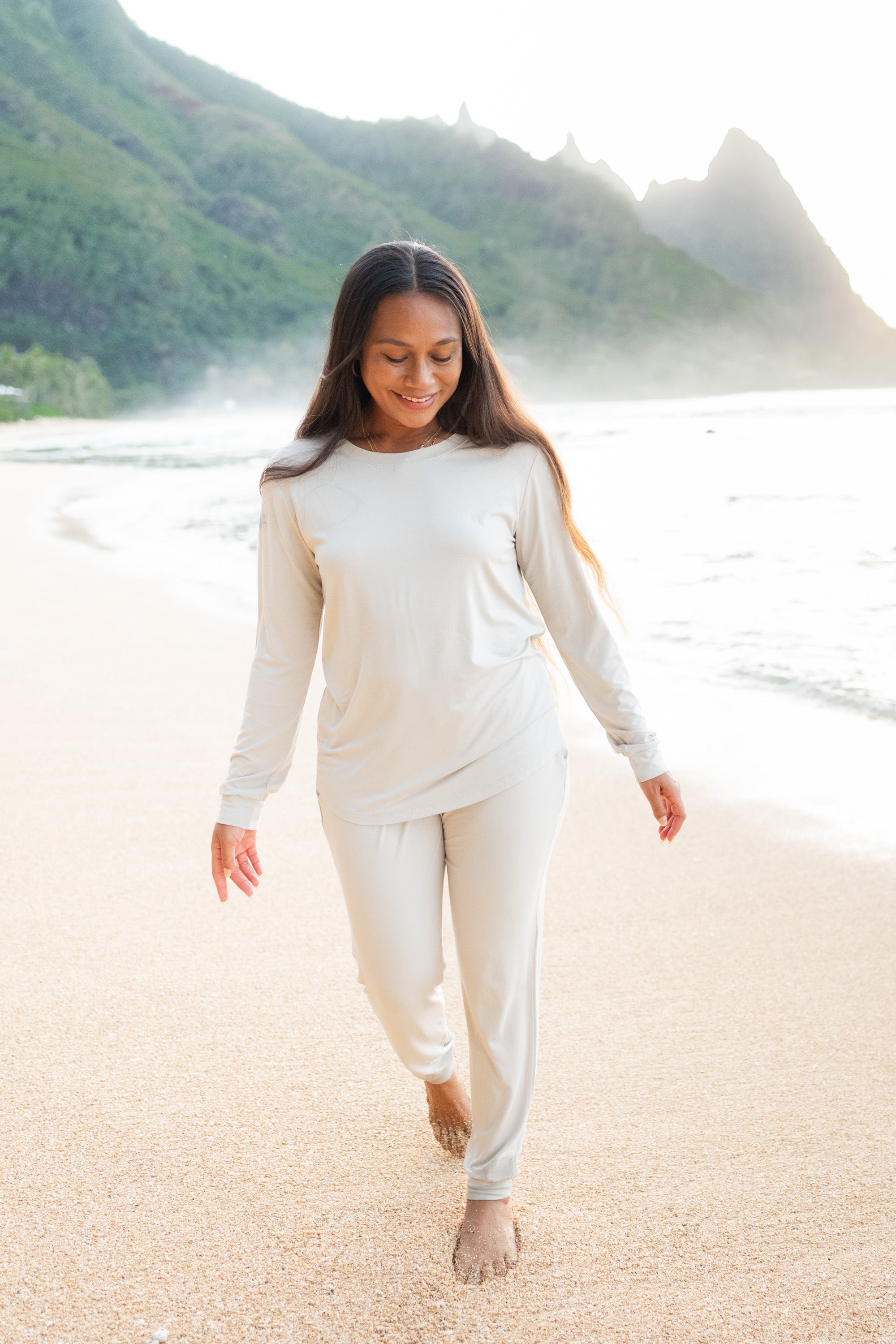 Model in the sand on the beach wearing Kyte Baby Women's Jogger Pajama Set in Oat