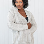 Model curled up in Chunky Cable Knit Cardigan in Oat