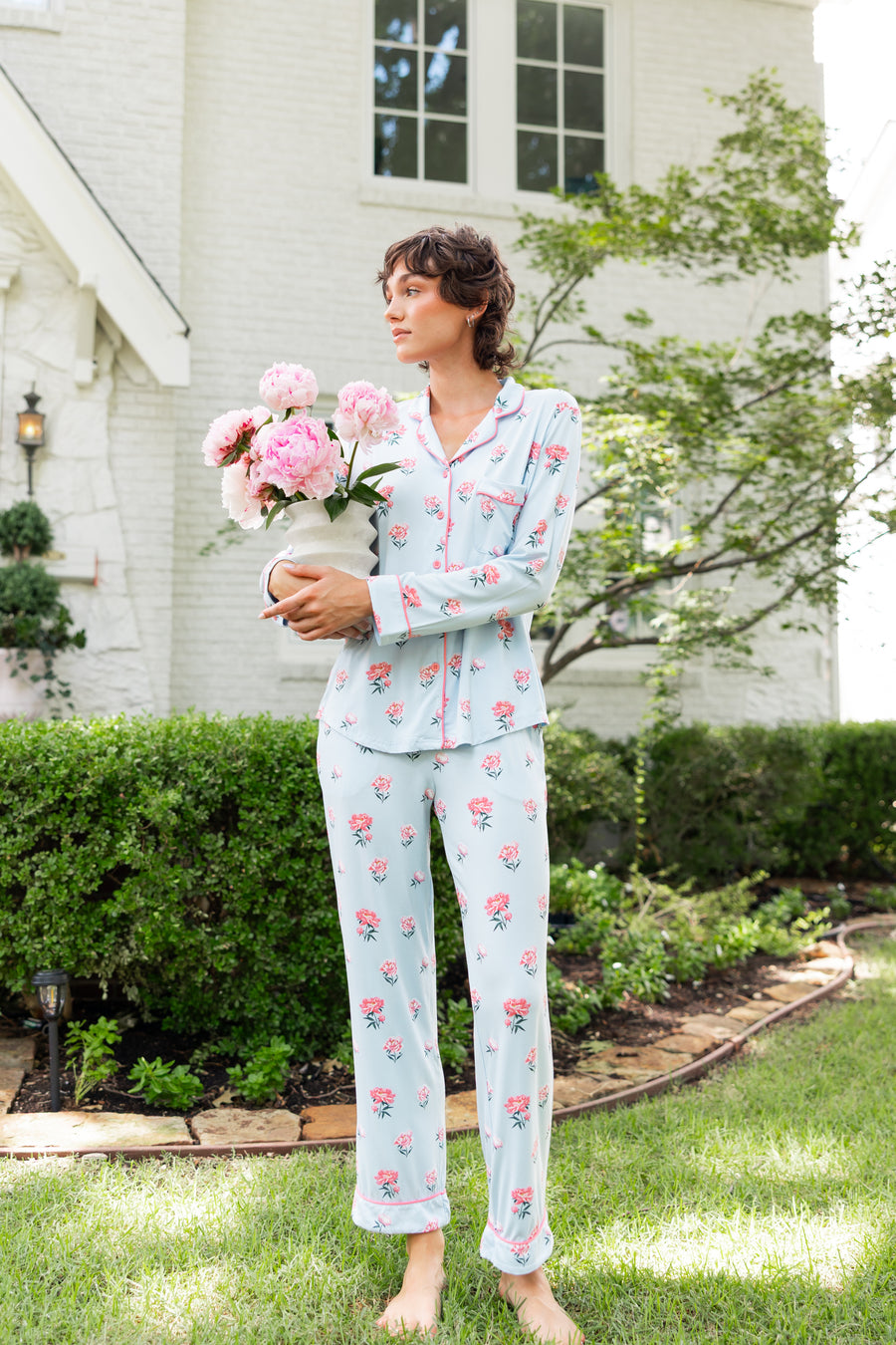Woman outside looking over holding a vase of flowers wearing long sleeve pajamas and pants in Peony on Breeze print.