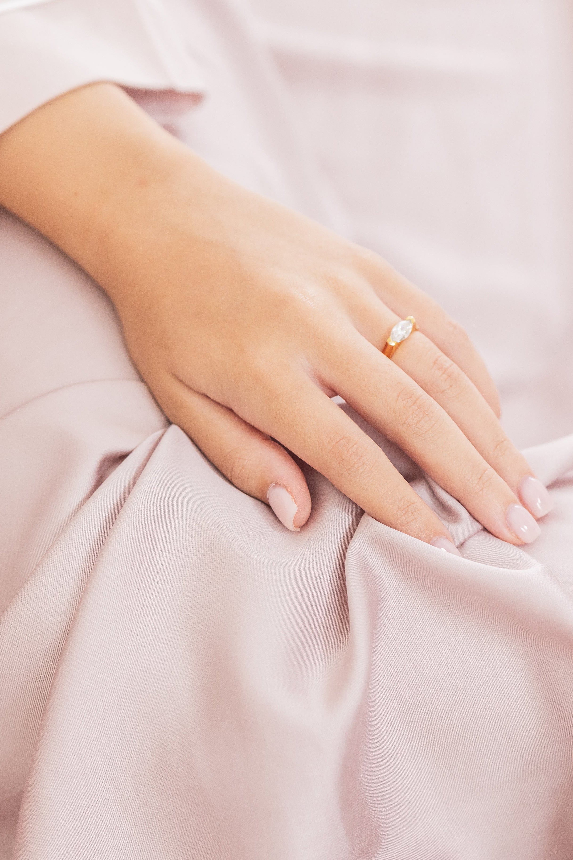 Hand with a ring on a soft pink fabric background