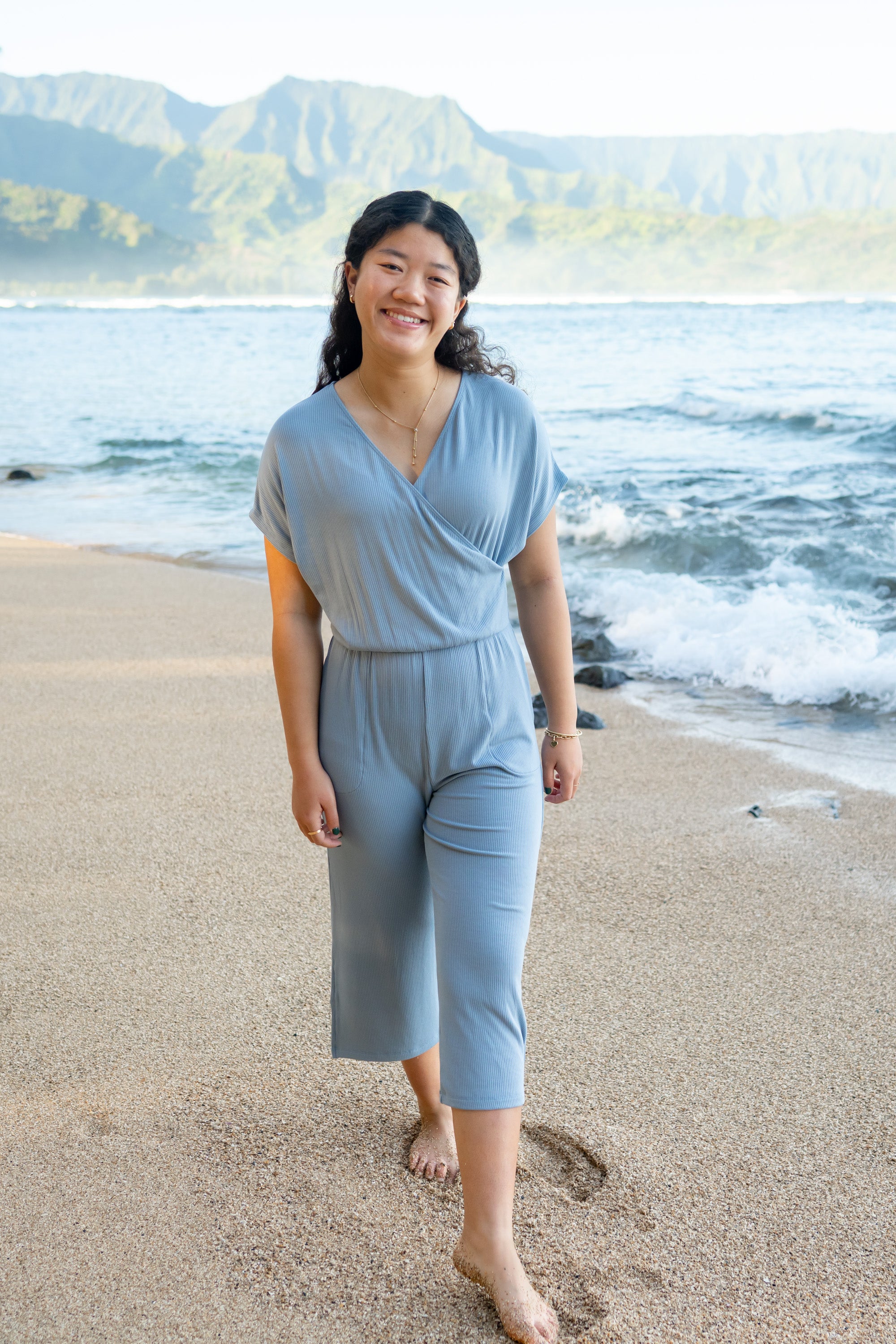 Smiling model walking on the beach wearing the Women's Ribbed Jumpsuit in Slate