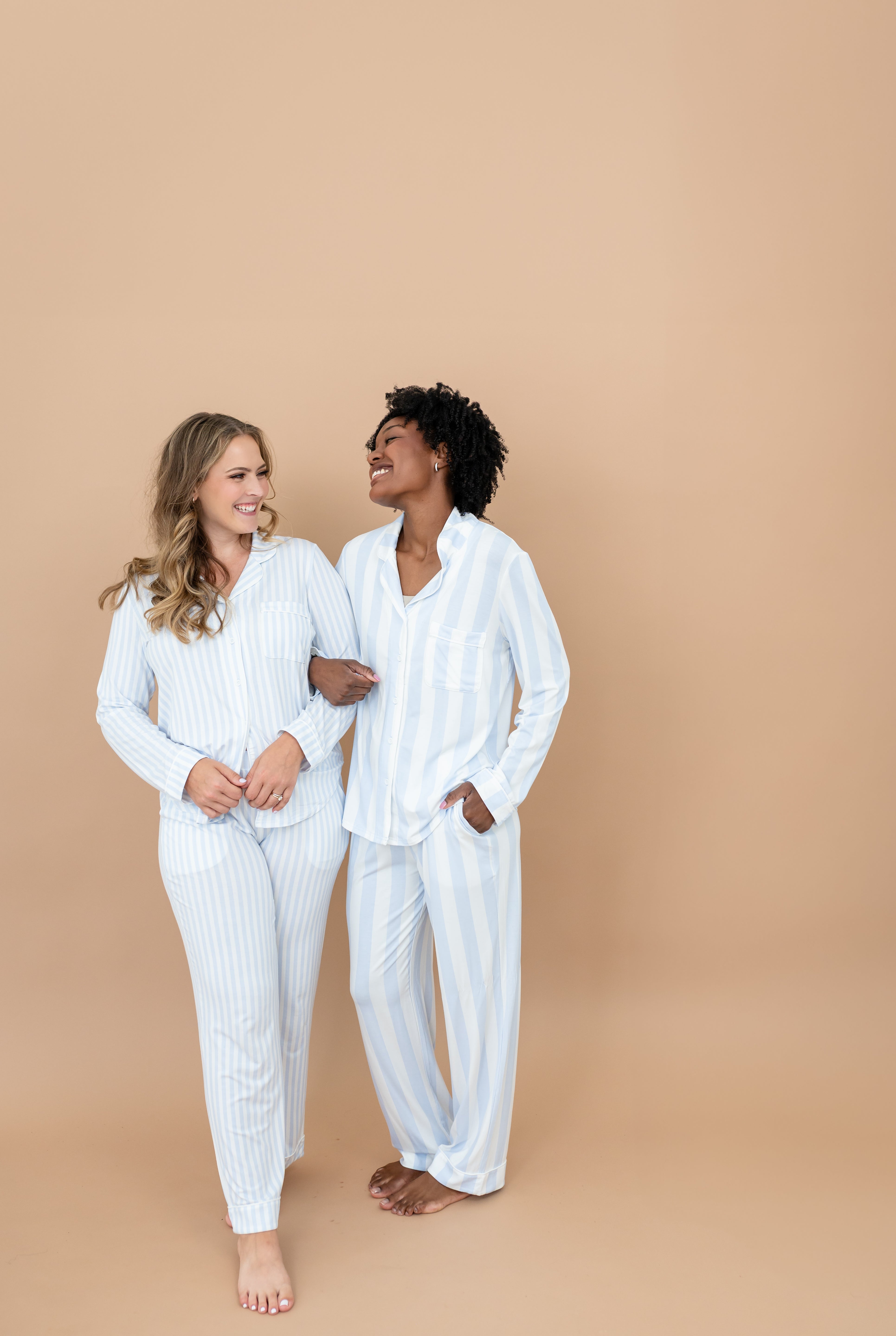 Two smiling female models standing side by side with their arms locked wearing the Long-Sleeved Women's Pajama Set in Small Mist Stripe and Big Mist Stripe