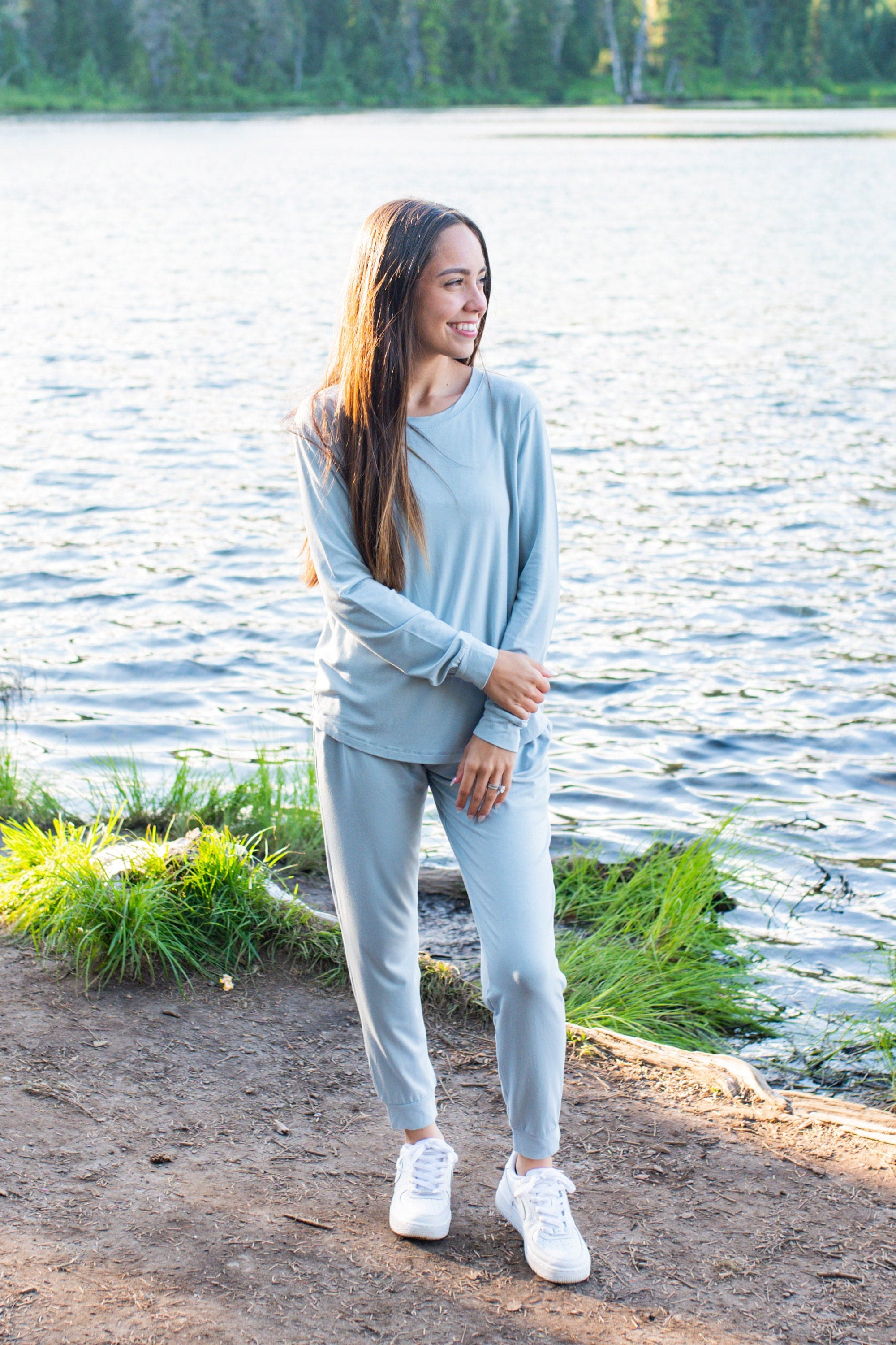 Woman modeling light blue jogger set in an outdoor setting with lake in backdrop