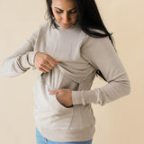 Female model lifting up the front of the Women's French Terry Nursing Hoodie in Almond while other hand is in pocket