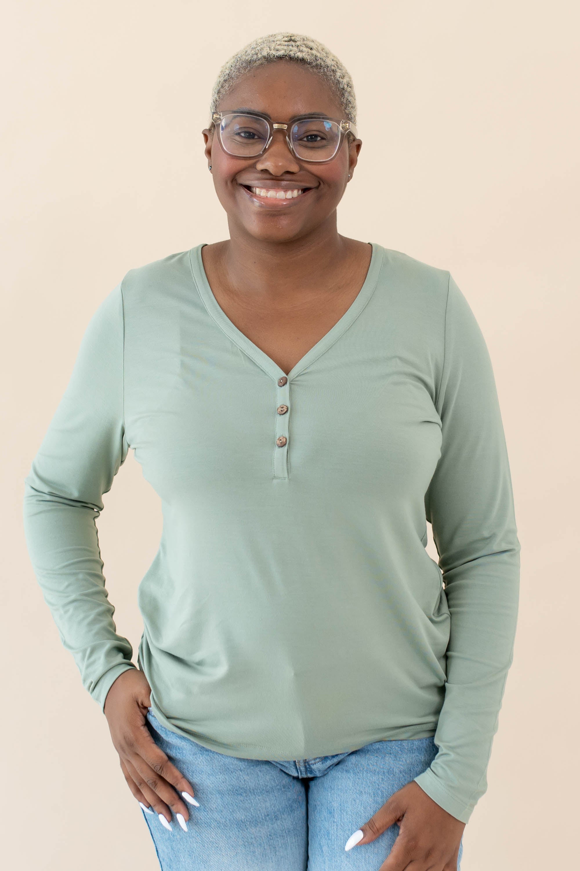 Model wearing the Women's Long Sleeve Henley Tee in Thyme paired with jeans
