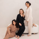Models sitting and standing on a white couch wearing the Bamboo Long-Sleeved Women's Pajama Sets in Latte with Latte Trim, Midnight with Midnight Trim and in Bisque with Bisque Trim