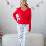 Female model standing in front of a cream colored ottoman wearing the Women's Lounge Pants in Vintage Santa with a cardinal women's henley